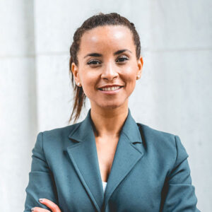 Person farbig, Portrait weiblich gelesen, braune Haare, lächelnd, blauer Blazer